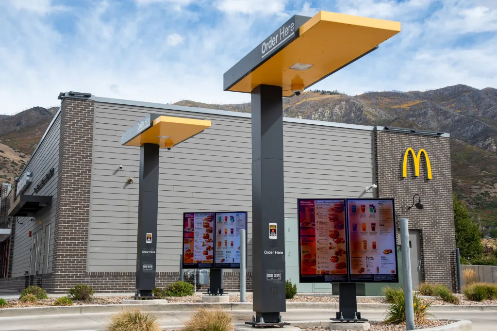 Digital menu boards in the empty drive-thru lanes of a McDonald's restaurant with a mountain background.