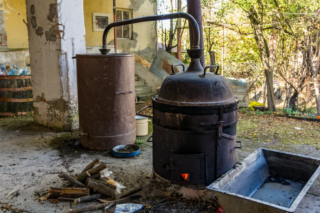 Distillation pot in a rural yard, used for crafting alcoholic beverages.