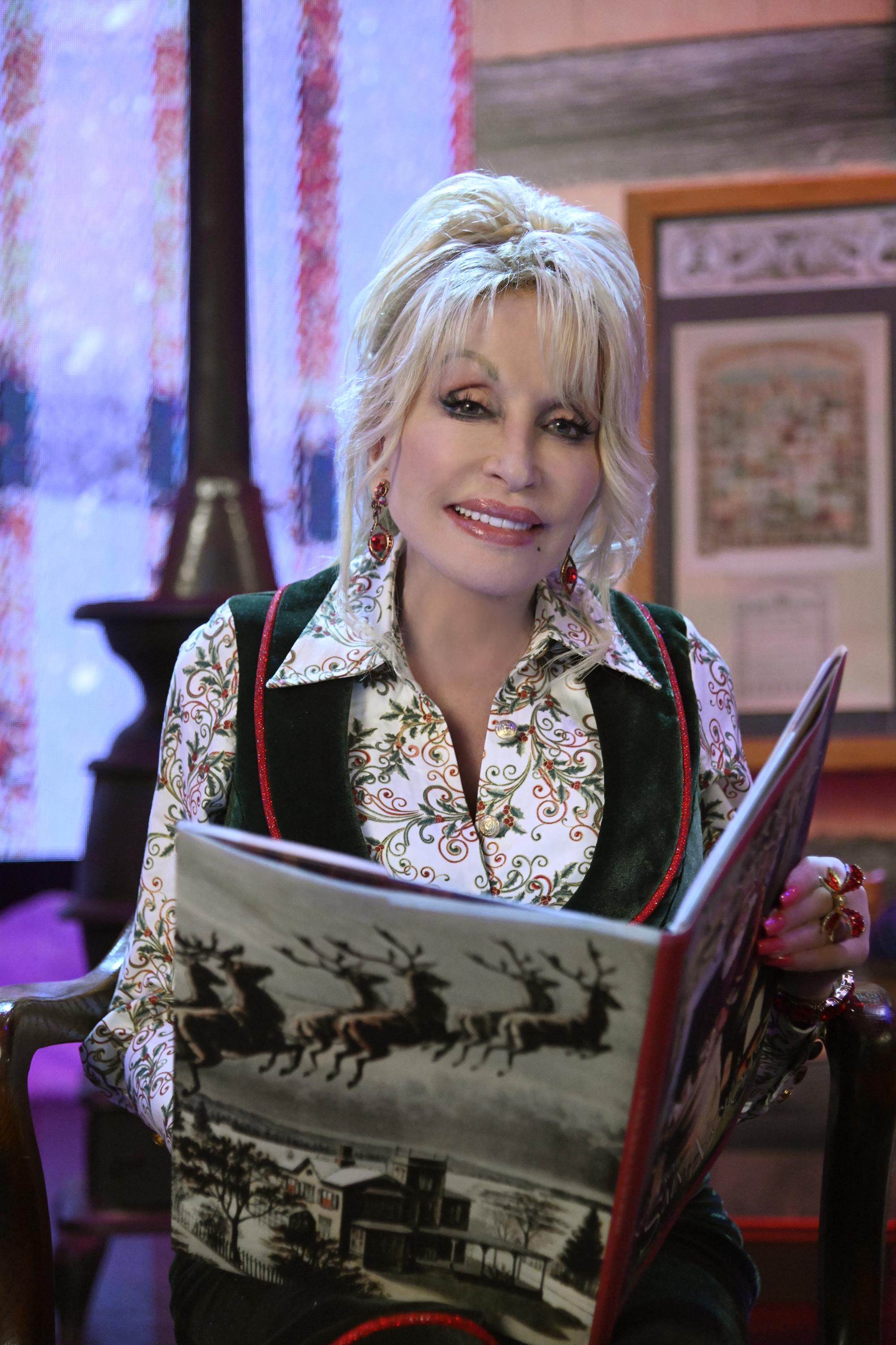 Dolly Parton reading a Christmas storybook, with Santa's reindeer flying over a snowy house on the cover.