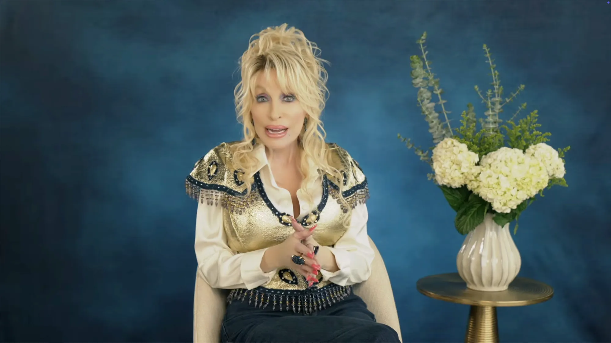 Dolly Parton accepts the Lifetime Achievement Award in a gold and blue embellished vest.