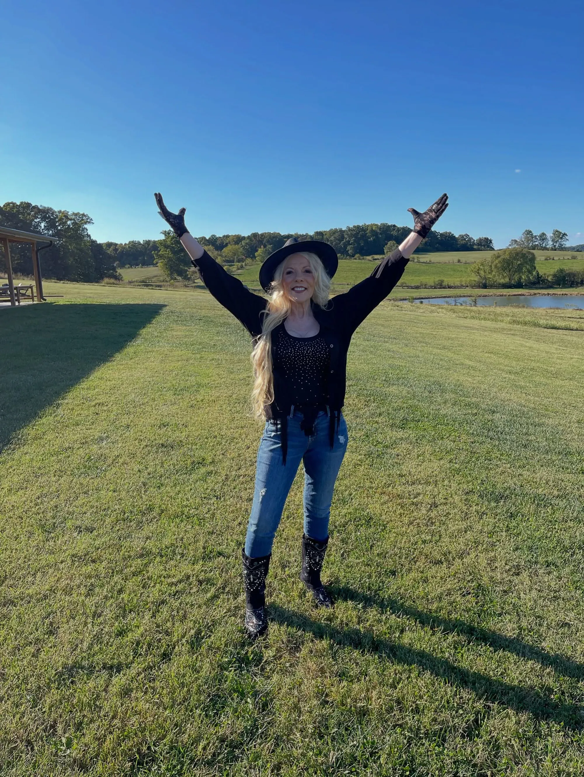 Frieda Parton stands in a grassy field with her arms raised.