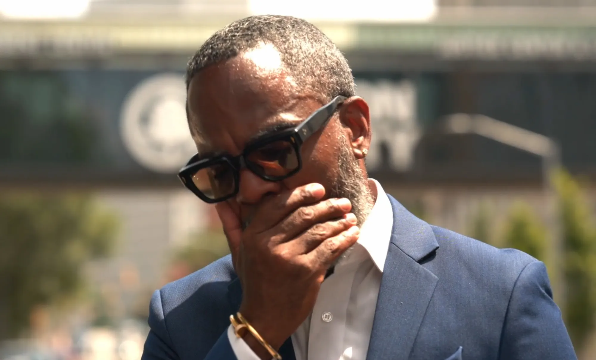 Man wearing glasses covers his mouth with his hand.