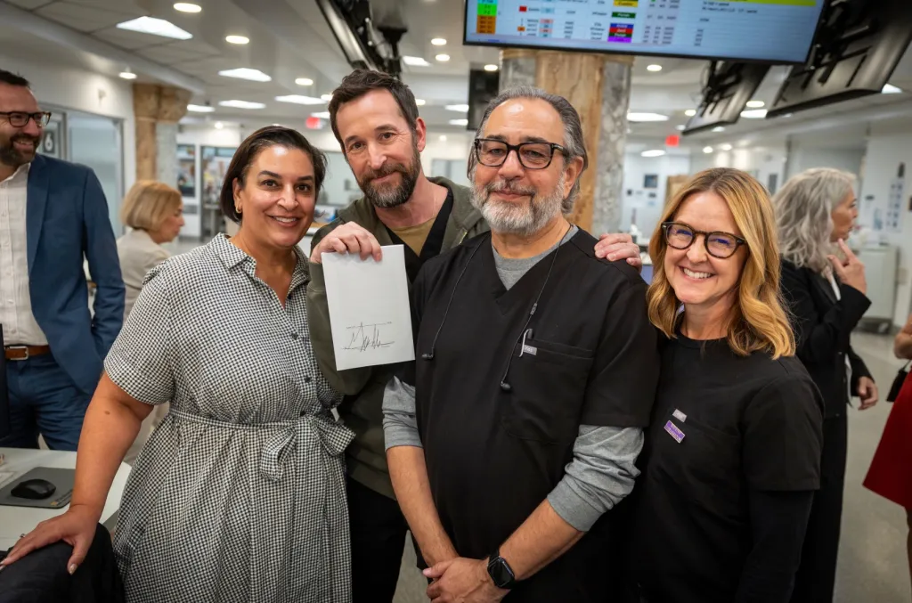 A group of four smiling people, three men and one woman, pose for a photo. One of the men holds a signed document.