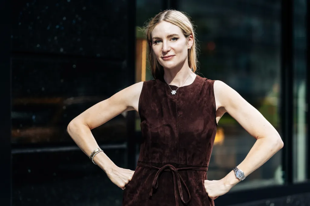 Dr. Amanda Kahn in a brown dress, standing with hands on her hips.