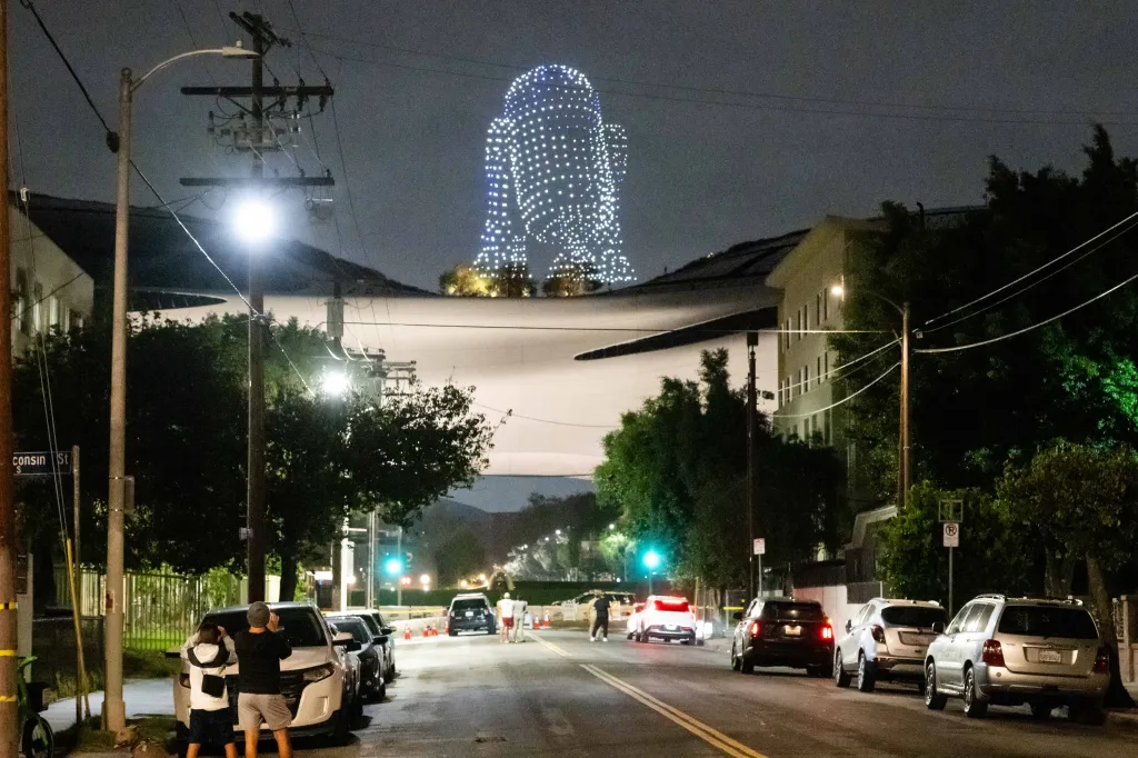 A drone show depicts the Star Wars character R2-D2 glowing in the night sky over a city street.