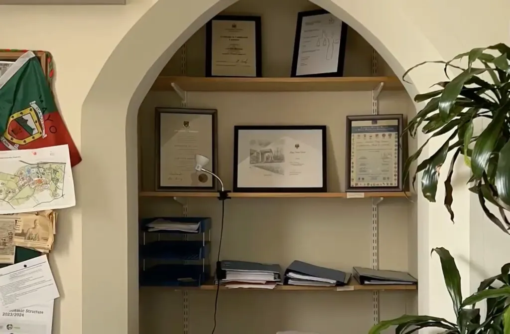 Shelves inside an arched wall recess in the Roebuck Castle building at University College Dublin display framed certificates and documents.