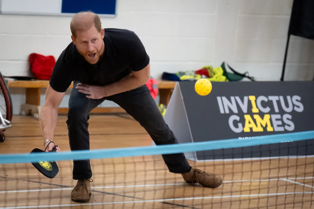 Prince Harry playing pickleball with a yellow ball, racket in hand, with an 