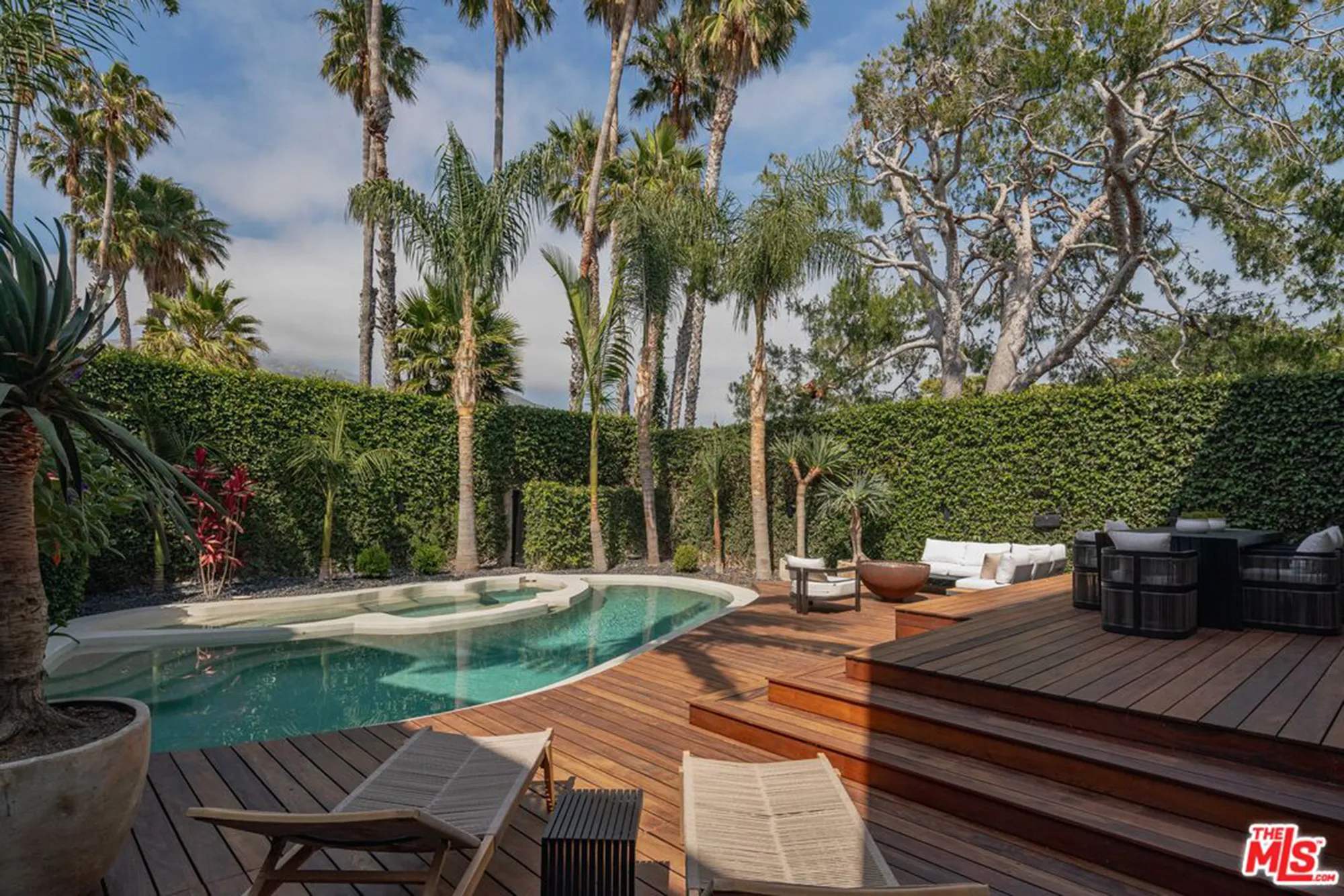 Backyard view of the $13M Malibu home with a pool, lounge chairs, patio, outdoor furniture, and palm trees.