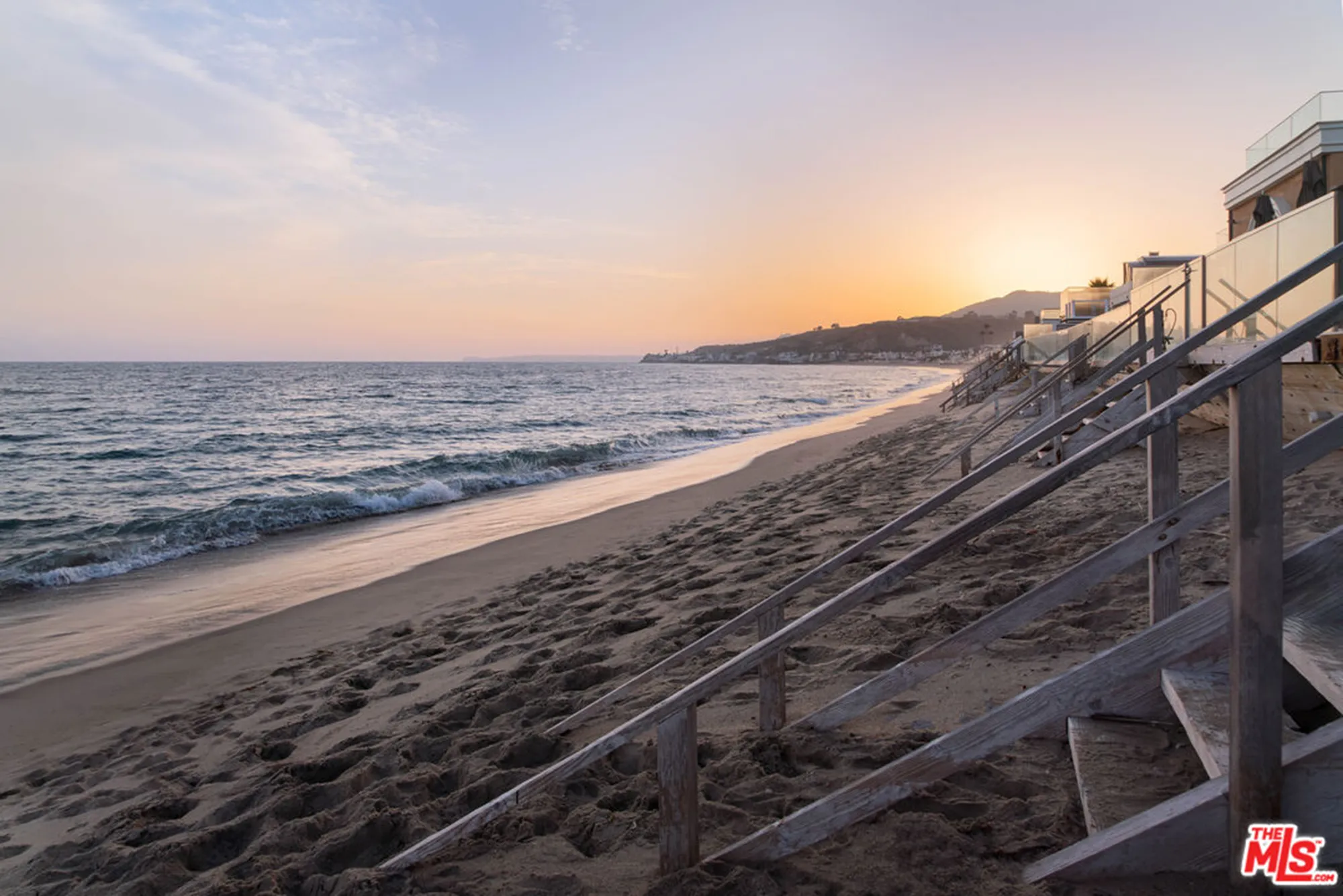 Beachfront Malibu home at sunset with stairs leading down to the sand.