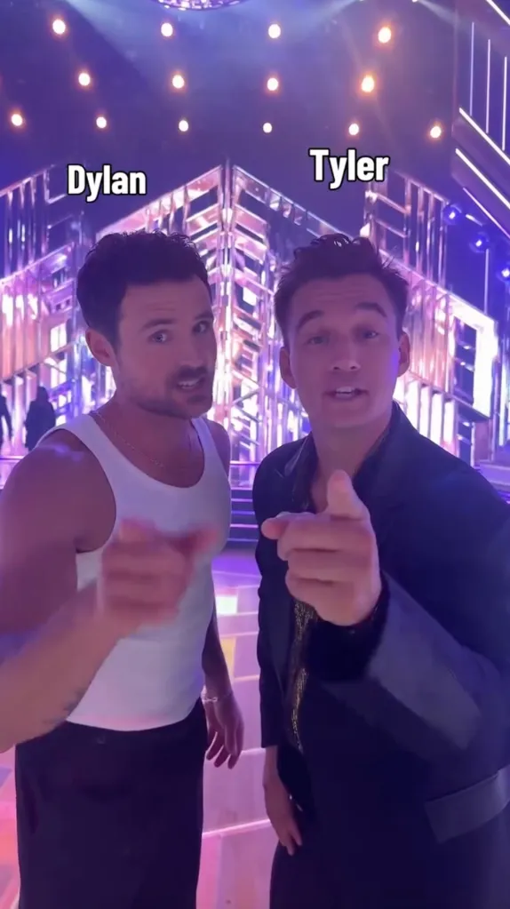 Dylan Efron and Tyler Cameron pointing at the camera on a purple-lit stage.