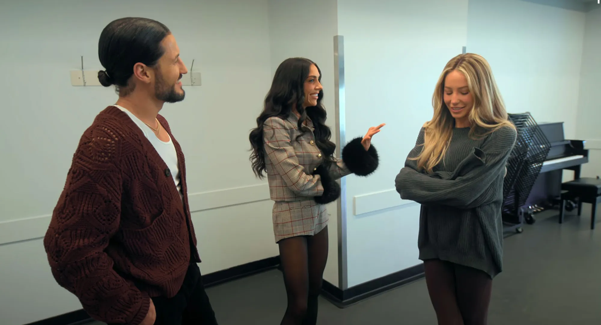 Three people, a man with a man bun and two women, talking in a room.