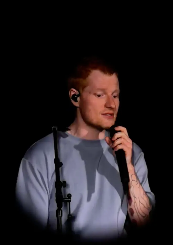 Ed Sheeran singing into a microphone on stage.