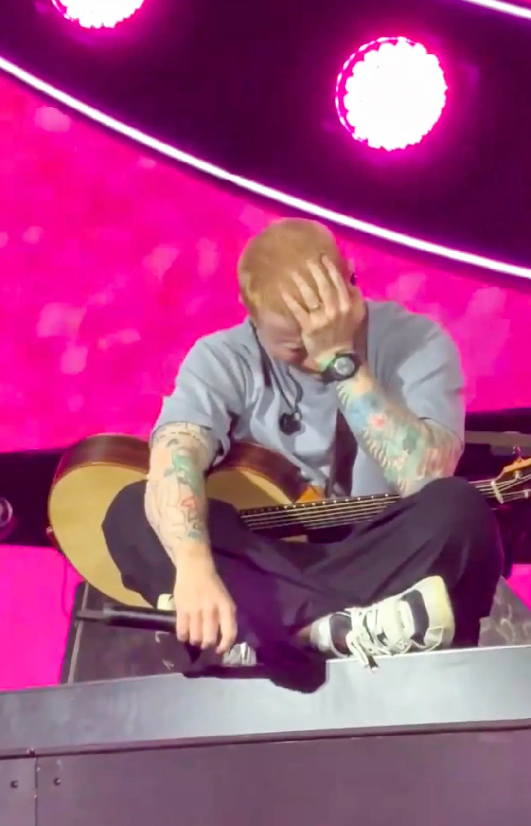 Ed Sheeran sits on stage, holding his head, appearing distressed during a concert in Philadelphia.