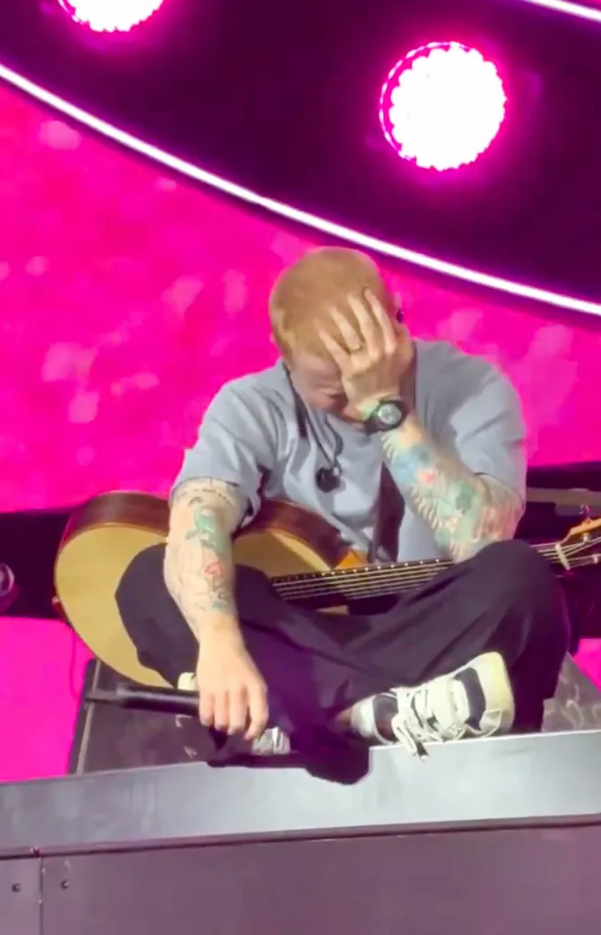 Ed Sheeran sits on stage, hand over his face, appearing to cry.