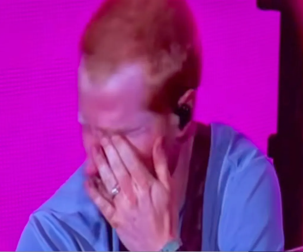 Ed Sheeran crying with his hands covering his face during a concert.