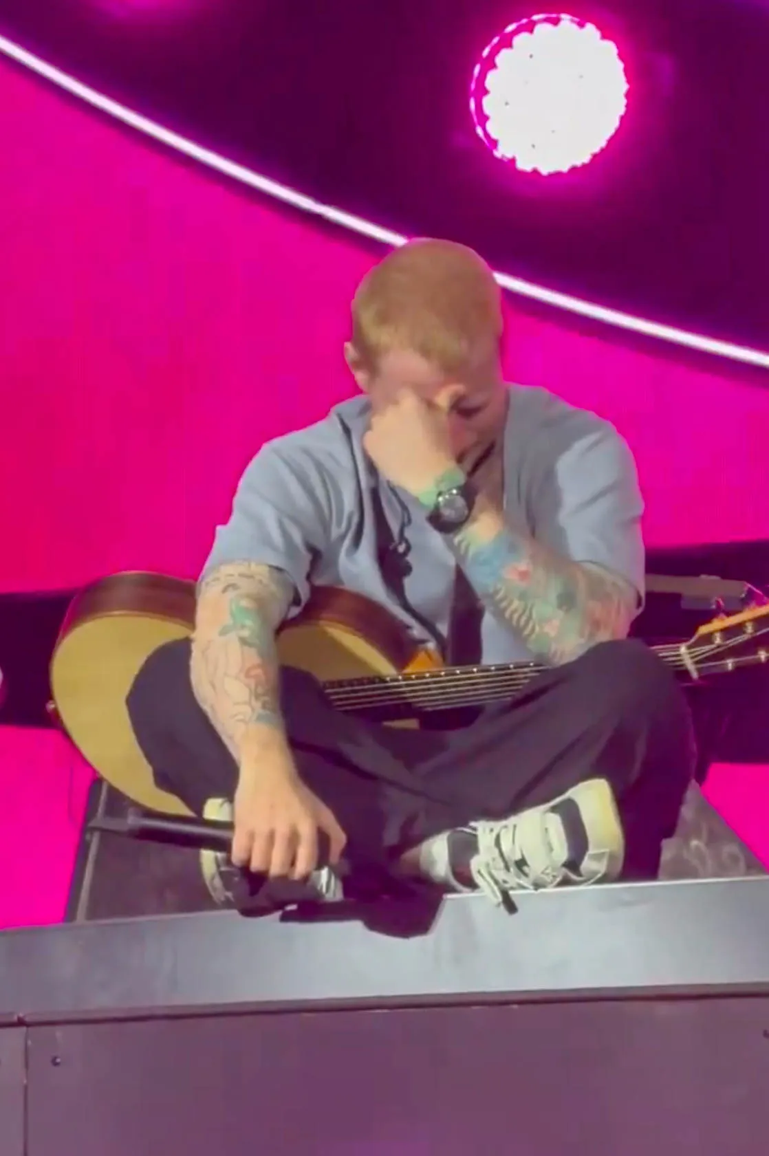 Ed Sheeran crying and holding an acoustic guitar during a concert in Philadelphia.