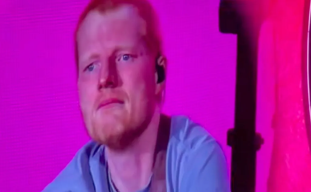 Ed Sheeran with an emotional expression on stage during a concert.