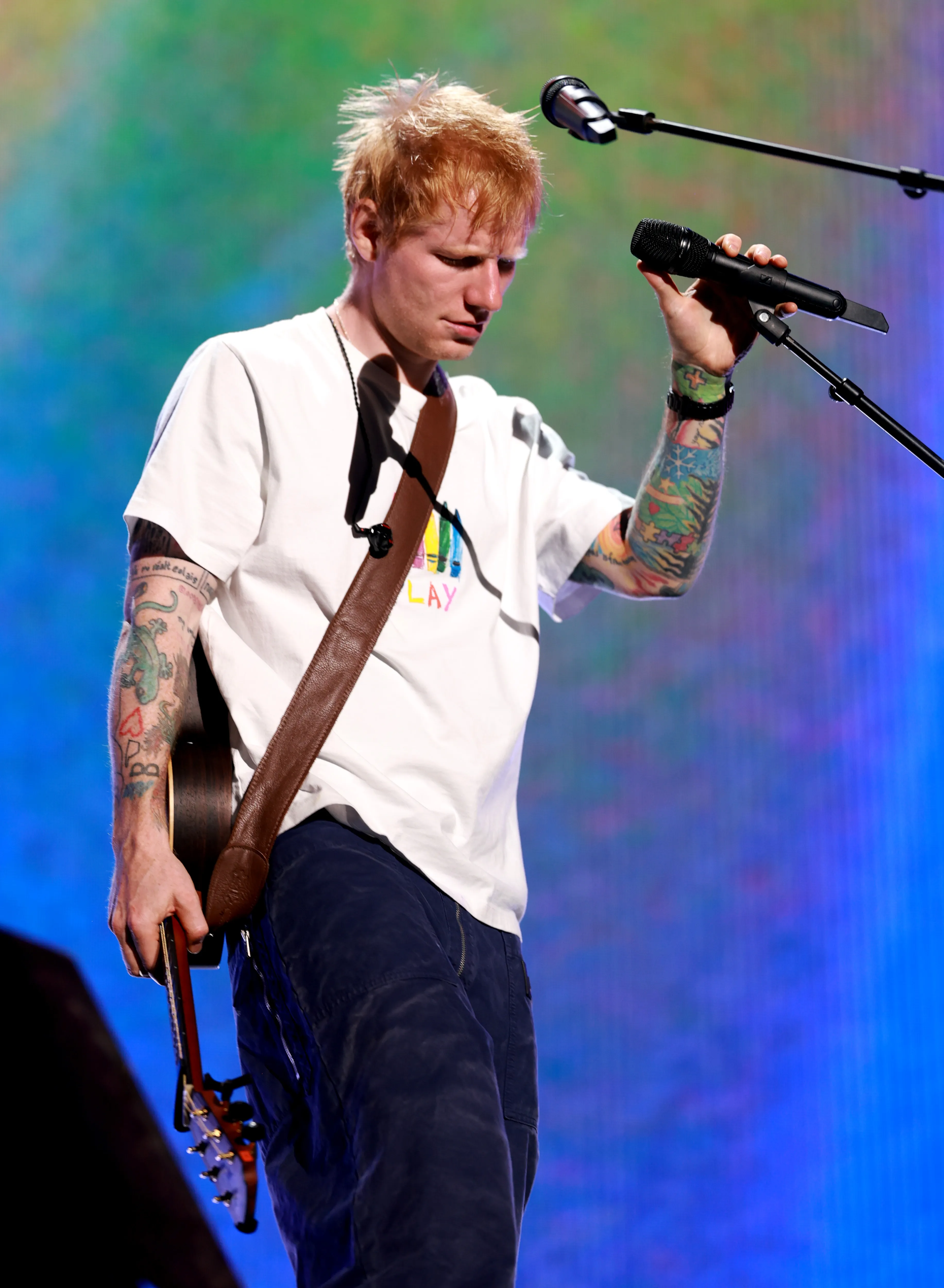 Ed Sheeran holding a microphone and a guitar during a performance.
