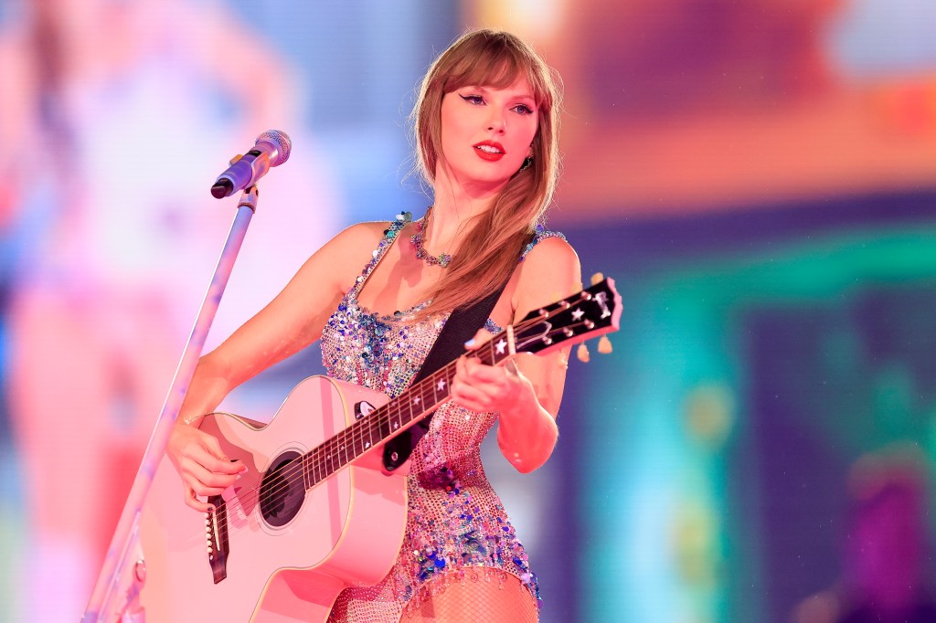 Taylor Swift performing on stage with a pink acoustic guitar and a microphone.