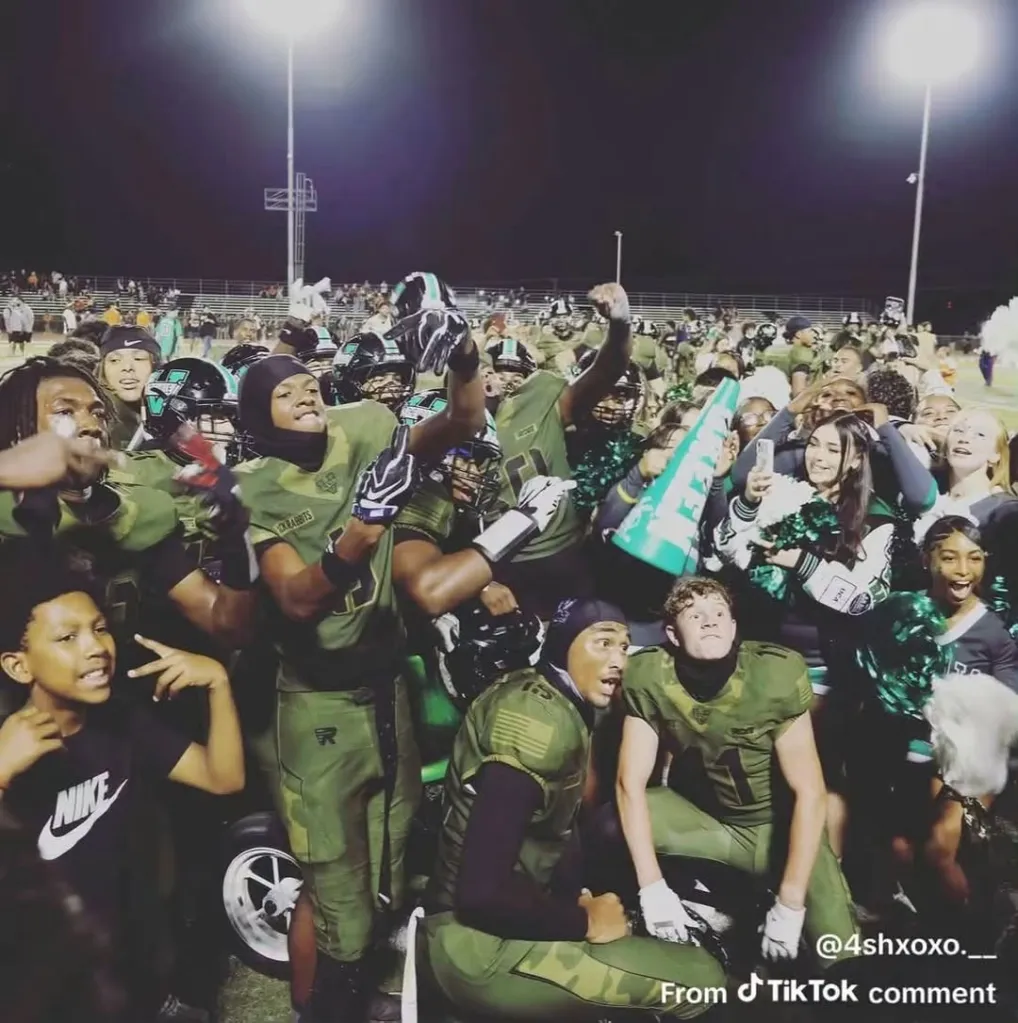 A California high school football team celebrating on the field with fans at night.