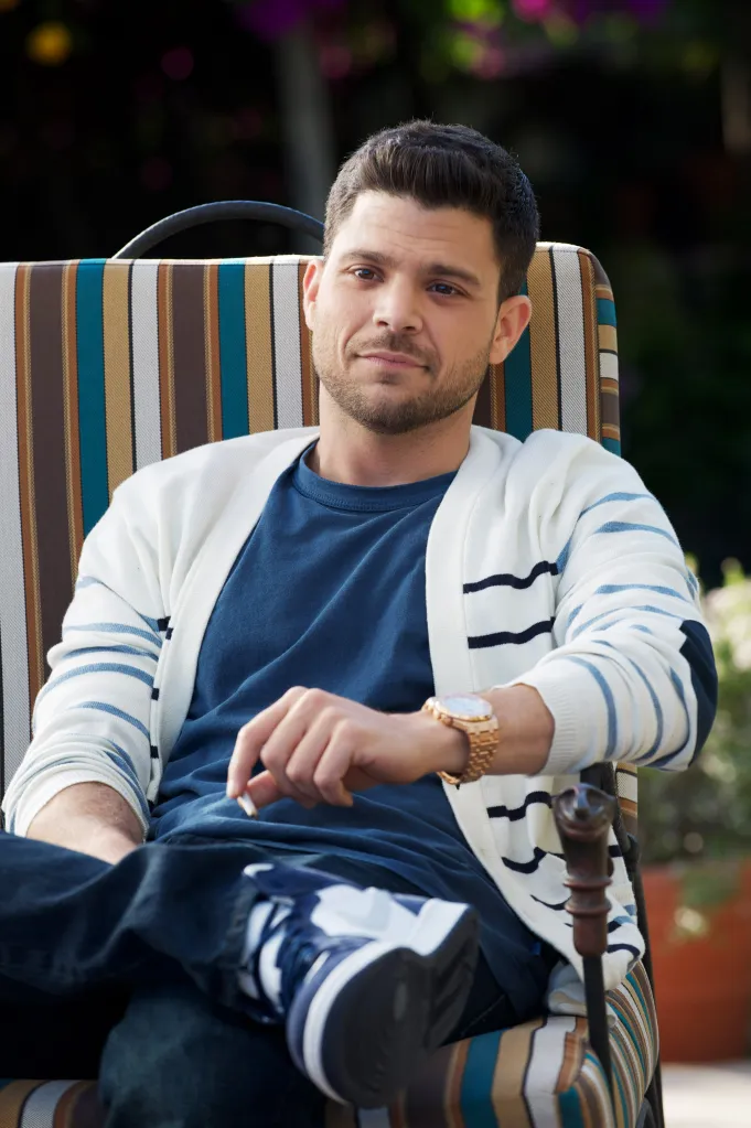 Jerry Ferrara sitting in a lounge chair wearing a cardigan, jeans, and sneakers.