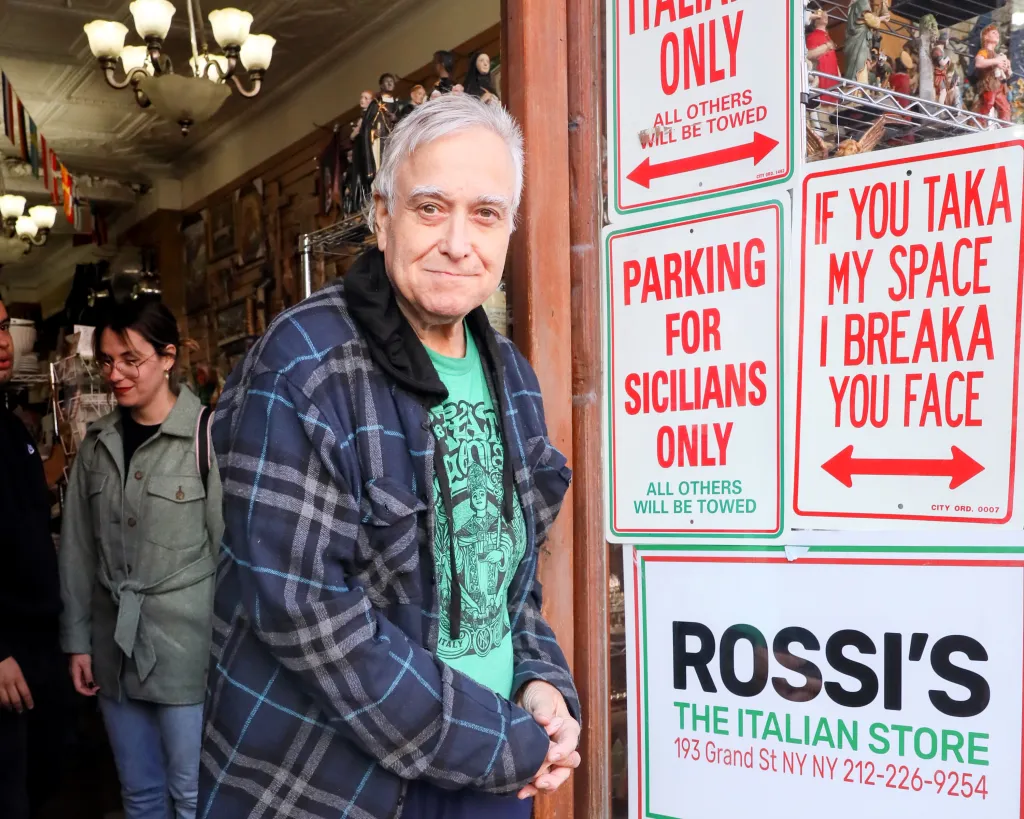 Ernest Rossi, owner of E. Rossi and Company, stands outside his store in Manhattan's Little Italy, next to signs in Italian colors.