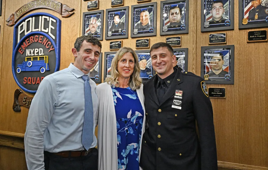 Nick D'Allara and his brother John, an ESU officer, with their mother Carol, in front of a memorial wall.