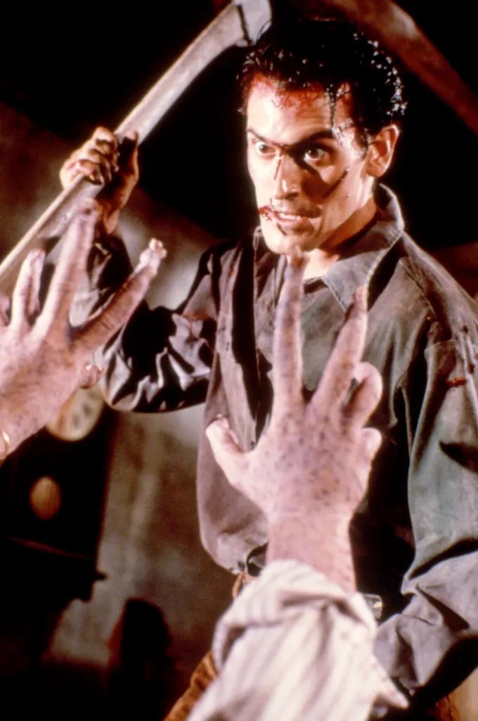 Bruce Campbell as Ash, bloody and holding an axe, facing monster hands in Evil Dead II.