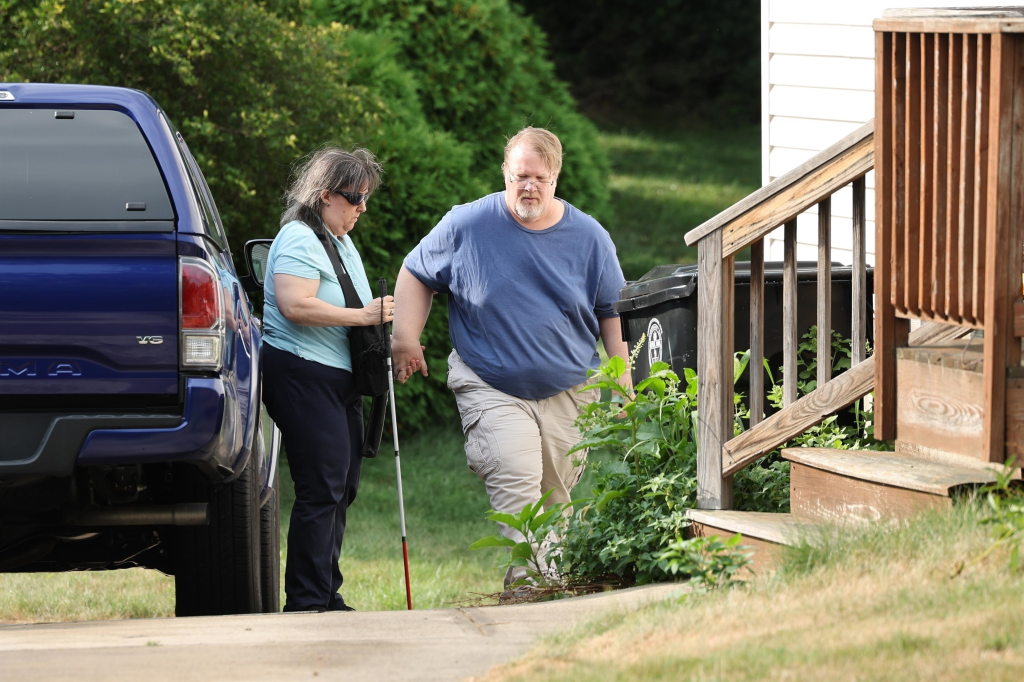 Matthew and Mary Crooks exiting their truck, with Mary holding a white cane, as they approach the steps to their home.