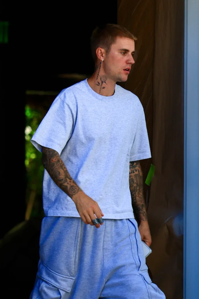 Justin Bieber wearing a gray t-shirt and gray sweatshorts, with visible tattoos on his arms and neck.