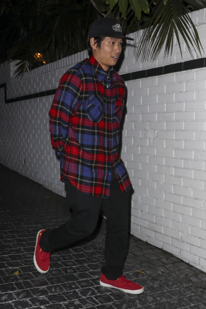 Pax Jolie-Pitt exiting the Chateau Marmont in a red and blue plaid shirt, black pants, red sneakers, and a black cap.