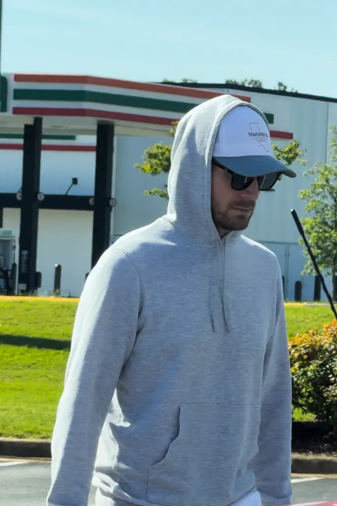 Brian Hickerson in a grey hoodie, sunglasses, and a hat, walking outdoors.