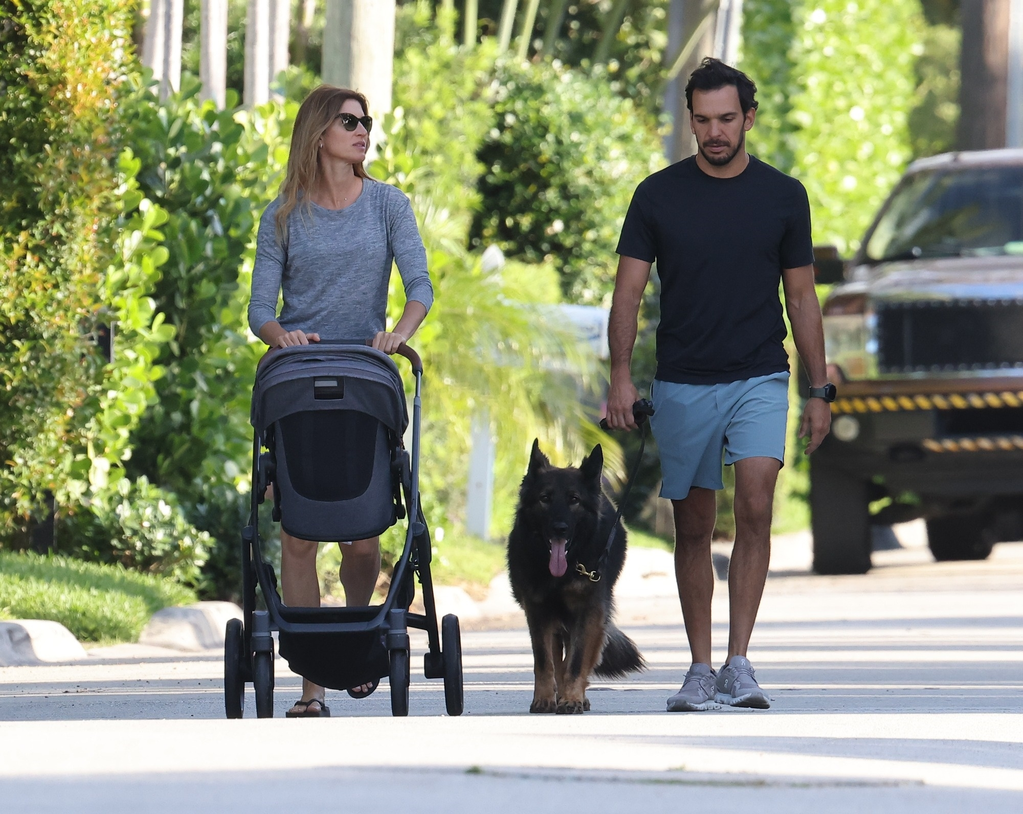 Gisele Bundchen pushing a stroller and Joaquim Valente walking a dog on a street.