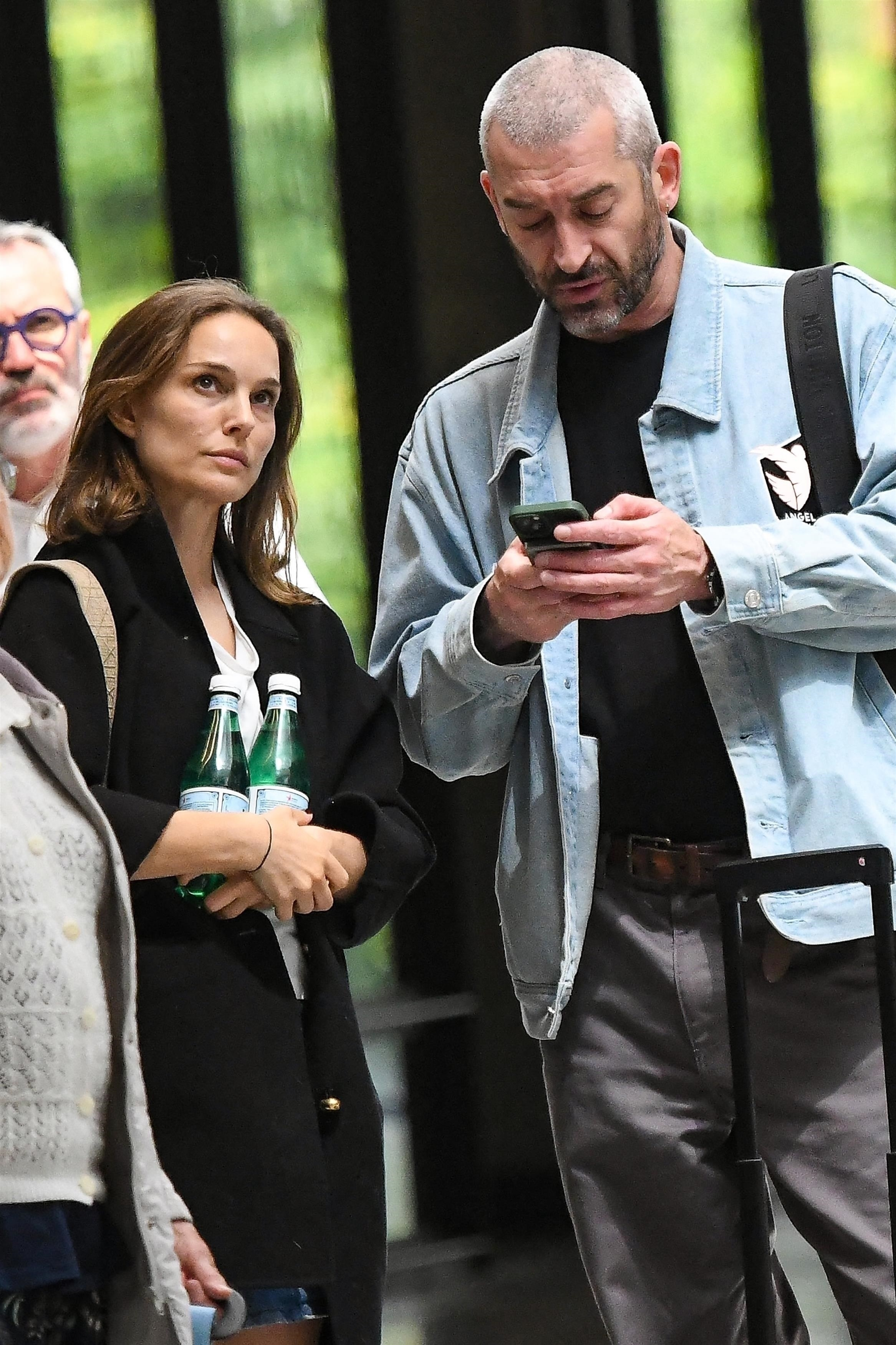 Natalie Portman holding water bottles next to Tanguy Destable, who is looking at his phone.