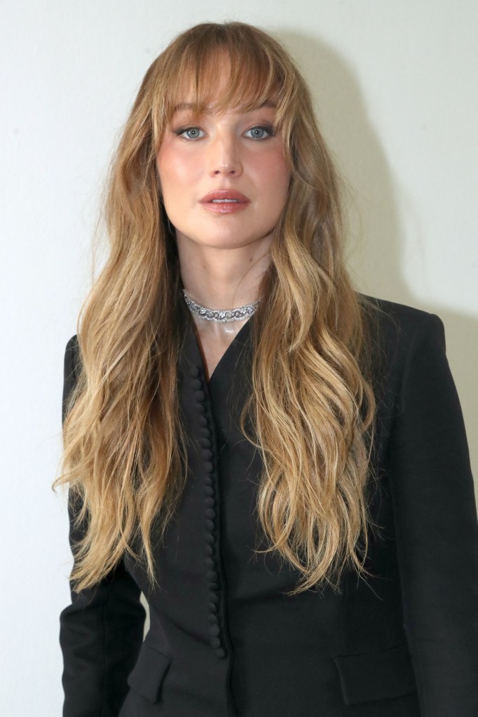 Jennifer Lawrence with long blonde hair and bangs, wearing a black blazer and a diamond choker.