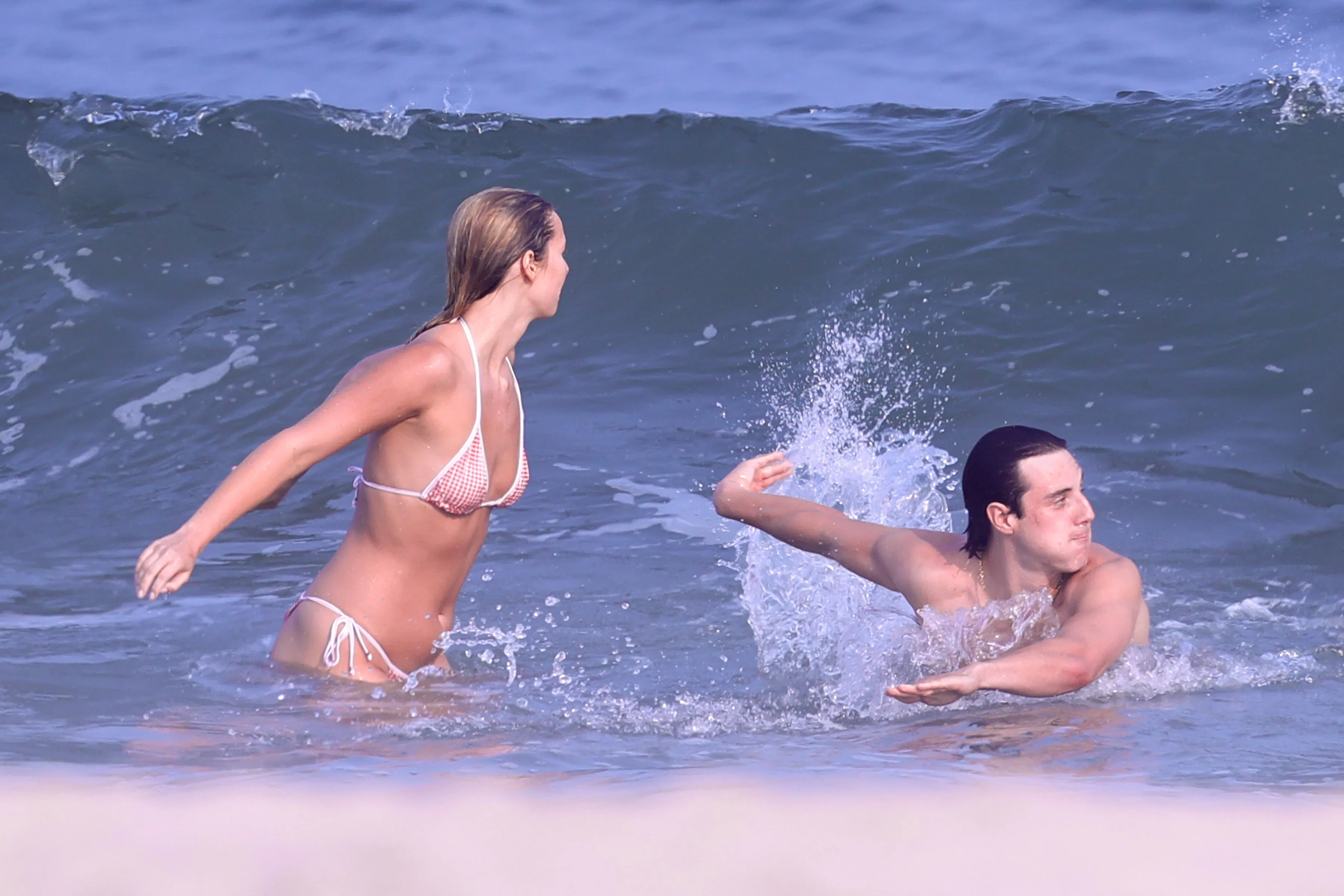 Apple Martin in a gingham bikini playing in the water with a man in the Hamptons.