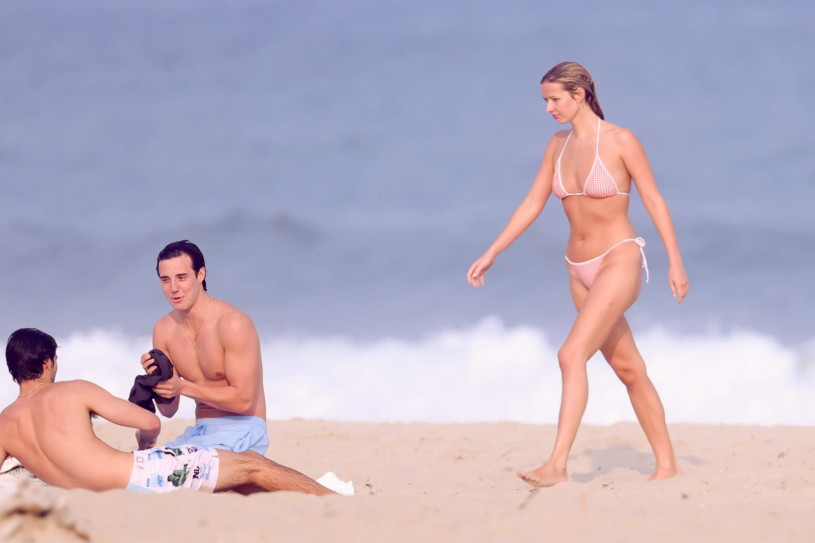 Apple Martin in a gingham bikini walking on the beach with Levi and another man.