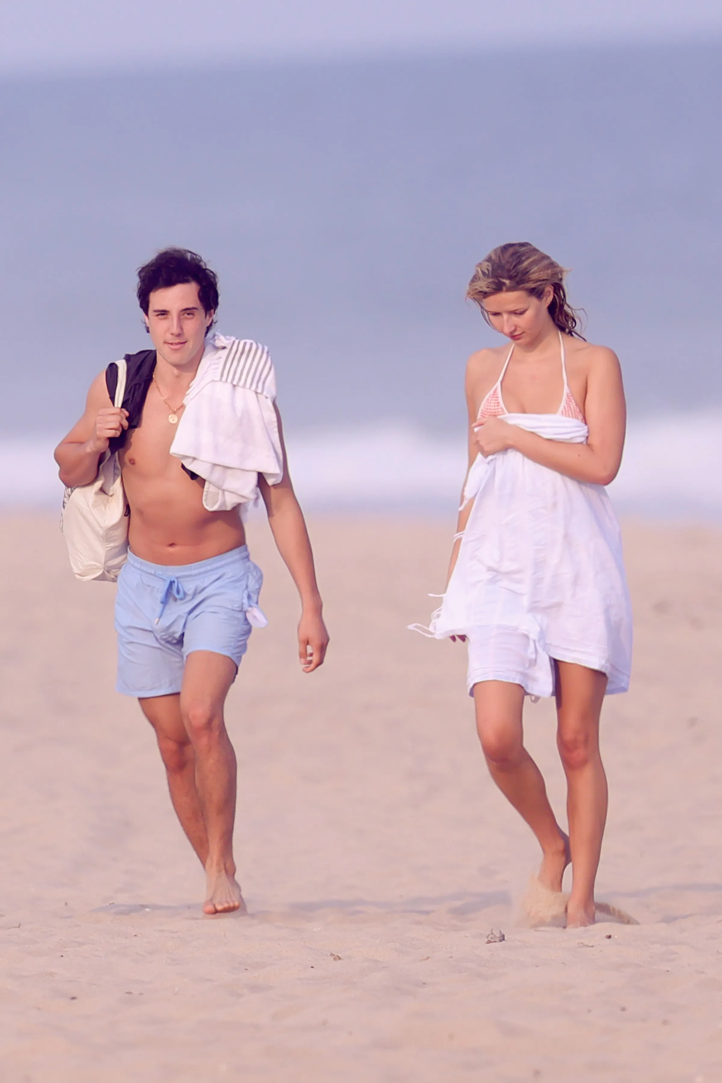 Apple Martin in a gingham bikini and a mystery man in swim trunks walking on the beach.