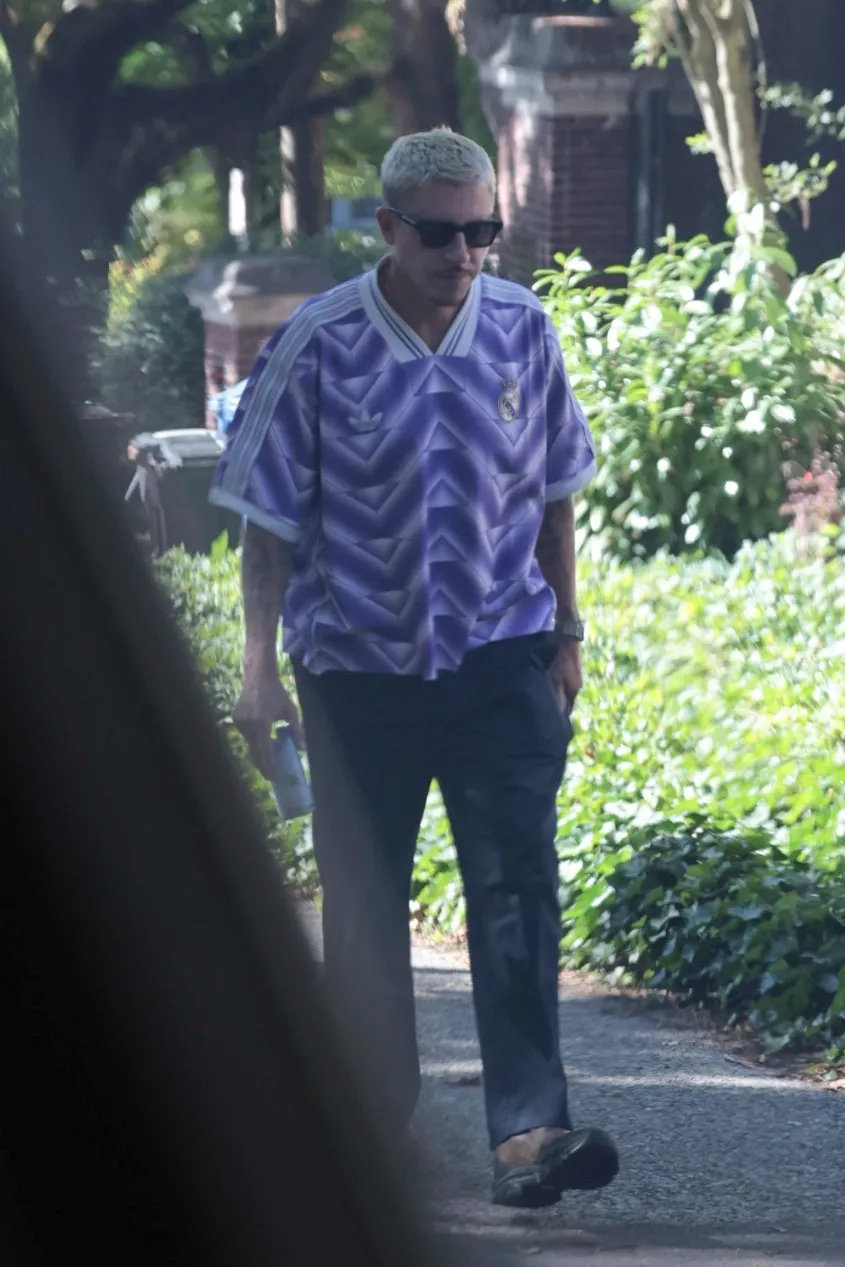 Macklemore walking outdoors in a purple Real Madrid soccer jersey and sunglasses.
