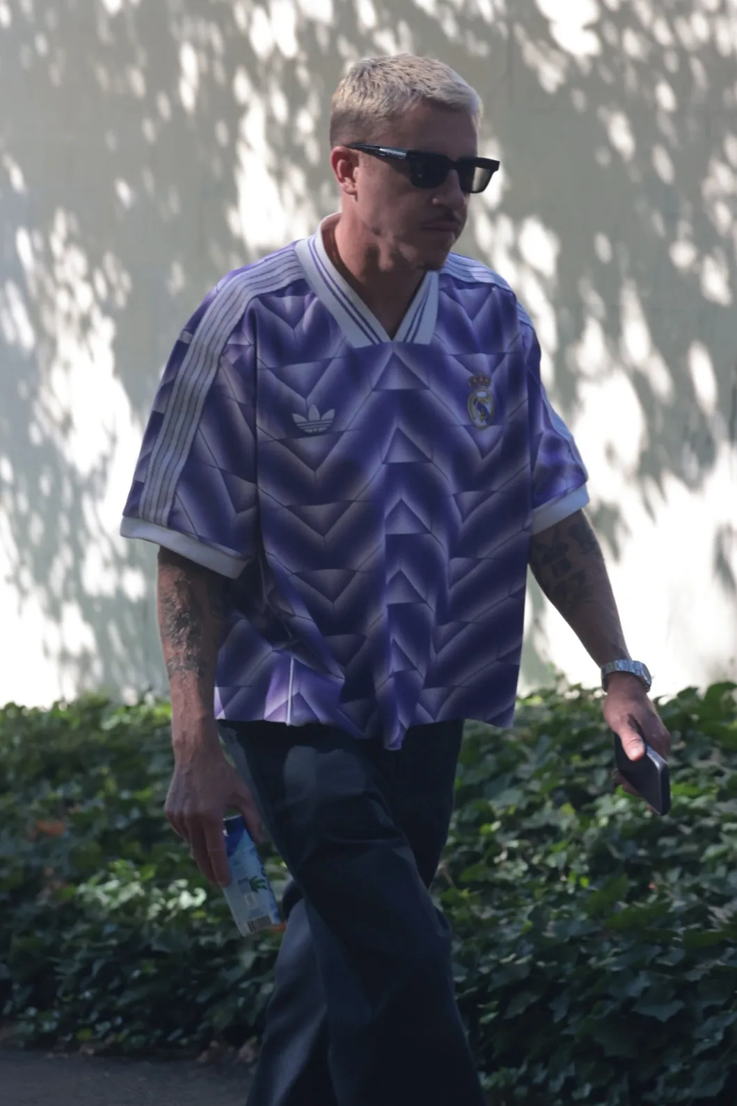 Macklemore wearing a purple Real Madrid soccer jersey and sunglasses, walking outdoors.