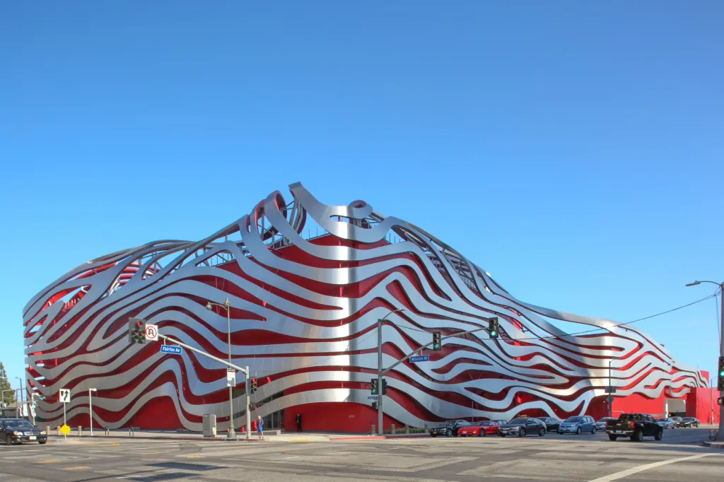 The Petersen Automotive Museum on Wilshire Boulevard, a red building with silver, wavy metal strips, at an intersection in Los Angeles.