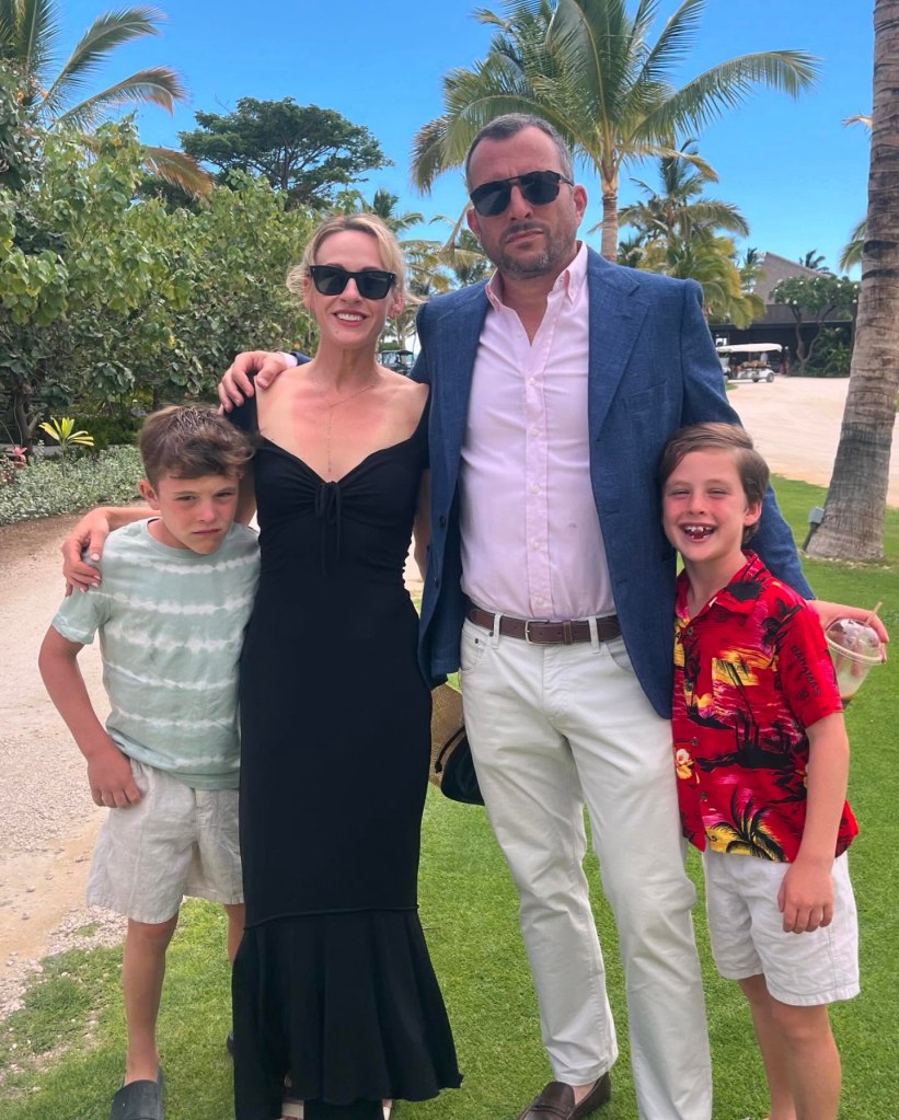 A couple in sunglasses standing with two young boys on a sunny day with palm trees in the background.