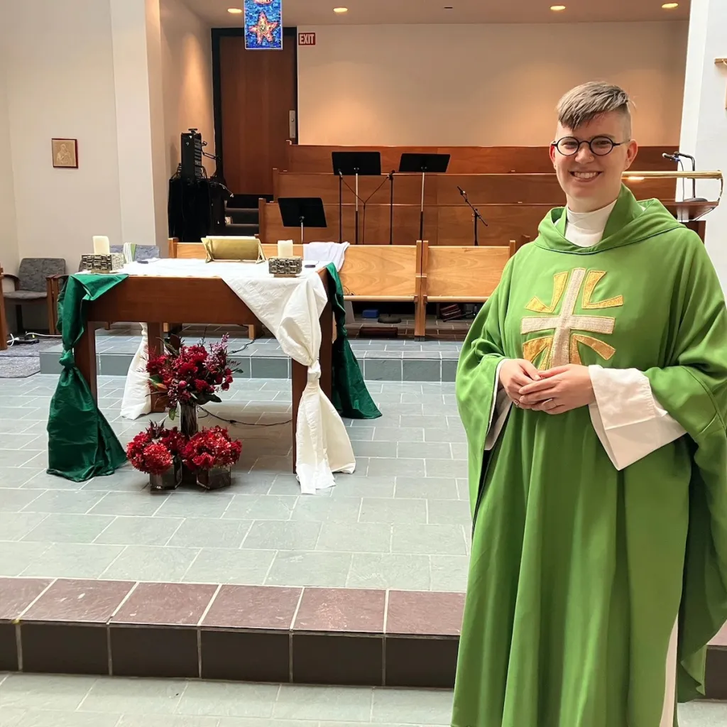 Father Flourish Klink, a nonbinary and transgender priest, smiling while wearing green vestments in a church.