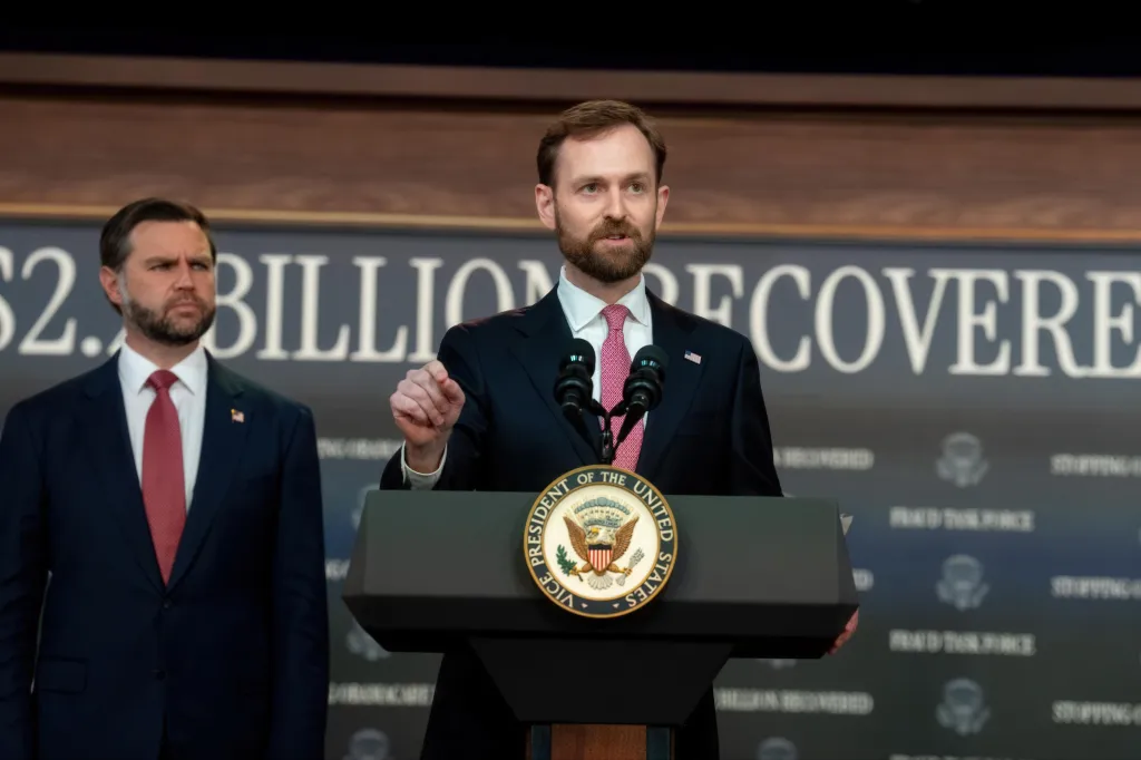 Federal Trade Commission Chair Andrew Ferguson speaking at a press conference, with Vice President J.D. Vance looking on.