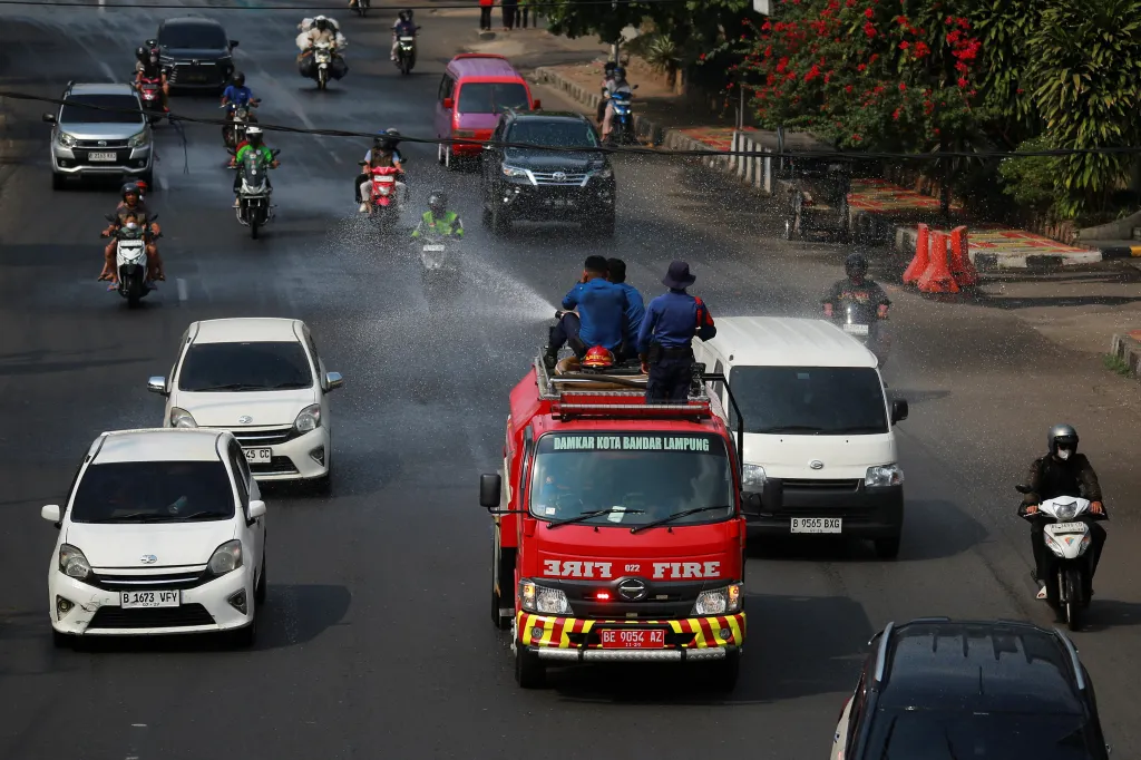 Firefighters spray water from a moving truck to clear volcanic ash from a road in Bandar Lampung.