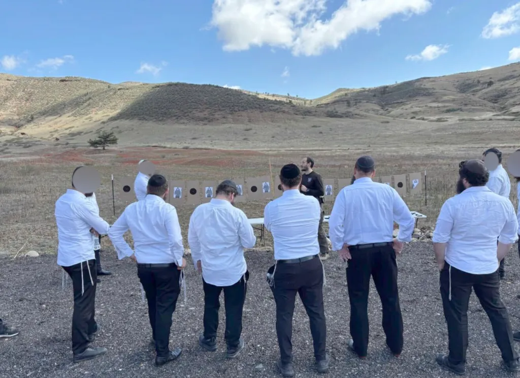 A group of men, identified as rabbis, attending firearm instruction and security training outdoors.