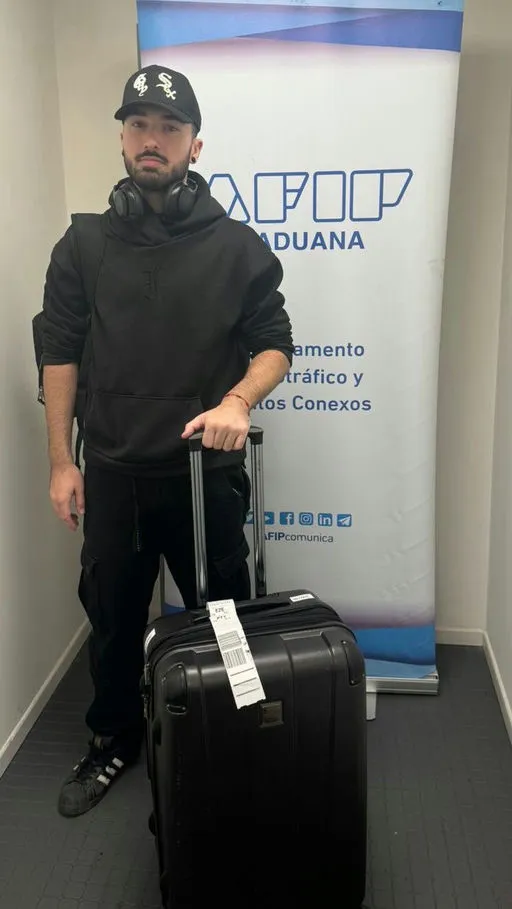 Braiden John Wilson with a rolling suitcase next to a banner from Argentina's customs office.