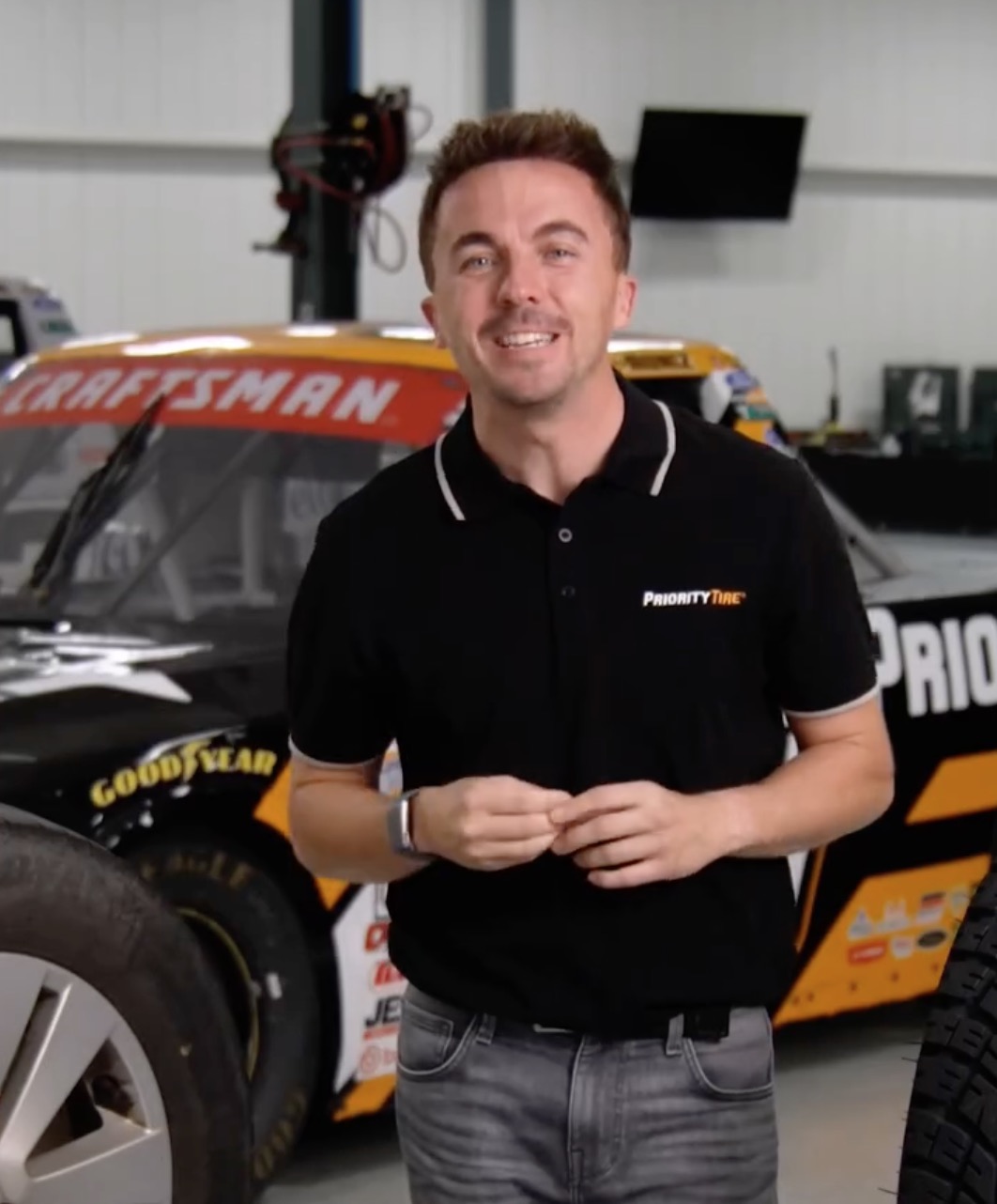 Frankie Muniz standing in front of a race car.