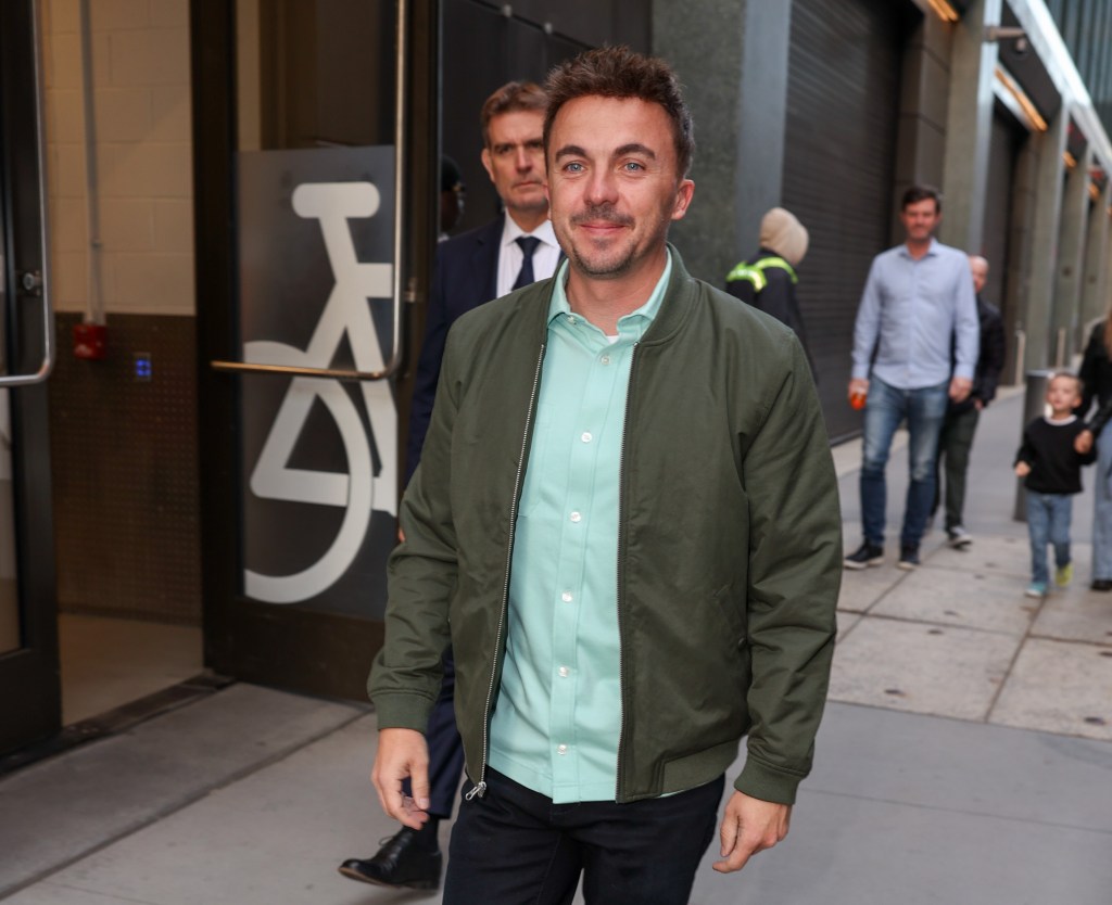 Frankie Muniz smiling, wearing a green bomber jacket and light blue collared shirt.