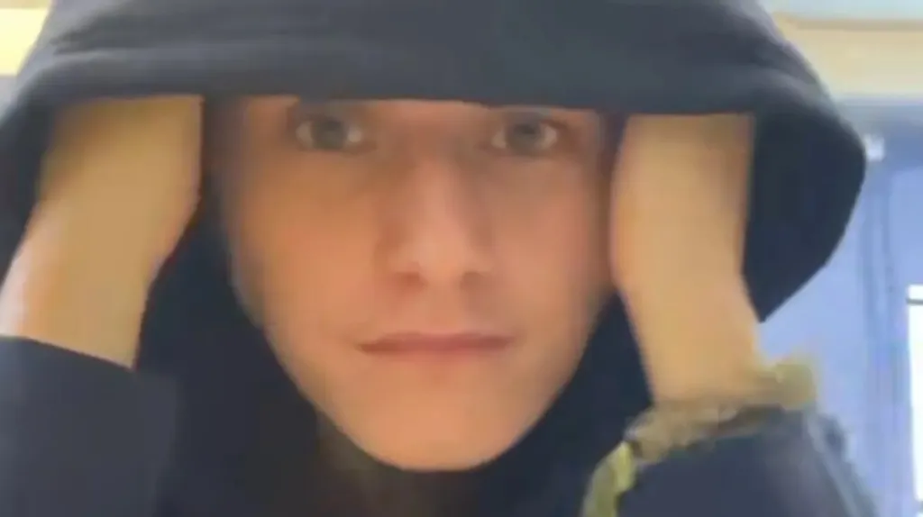A person pulling down a black hoodie with their hands, eyes looking directly forward.